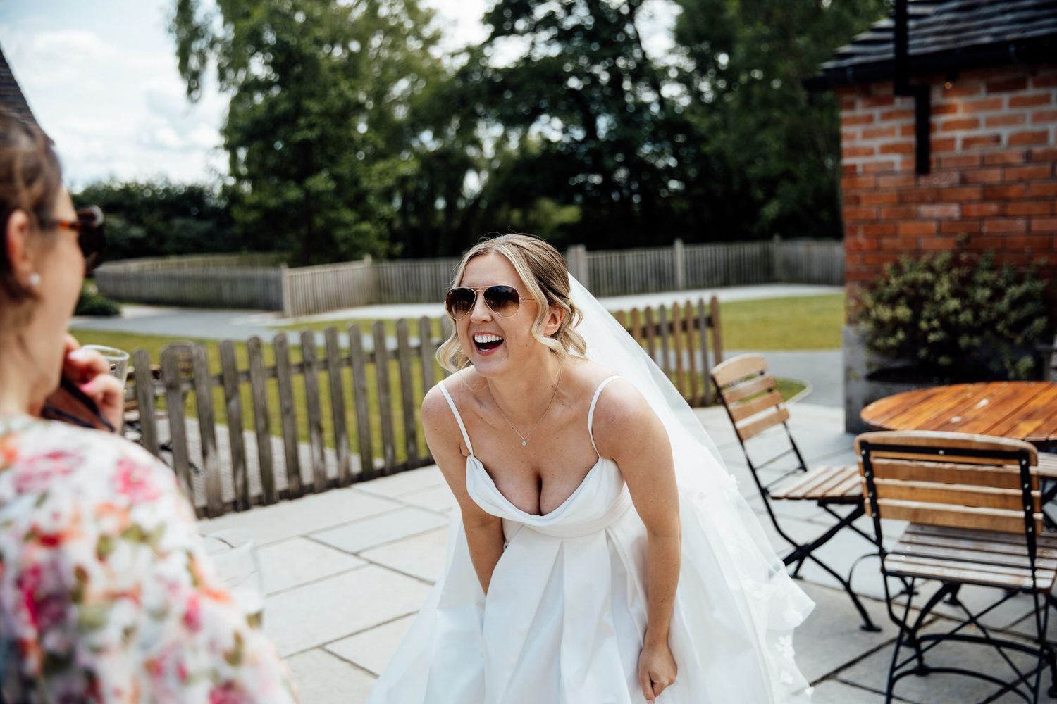 Wedding guests enjoying an outdoor reception on a sunny patio with brick walls.