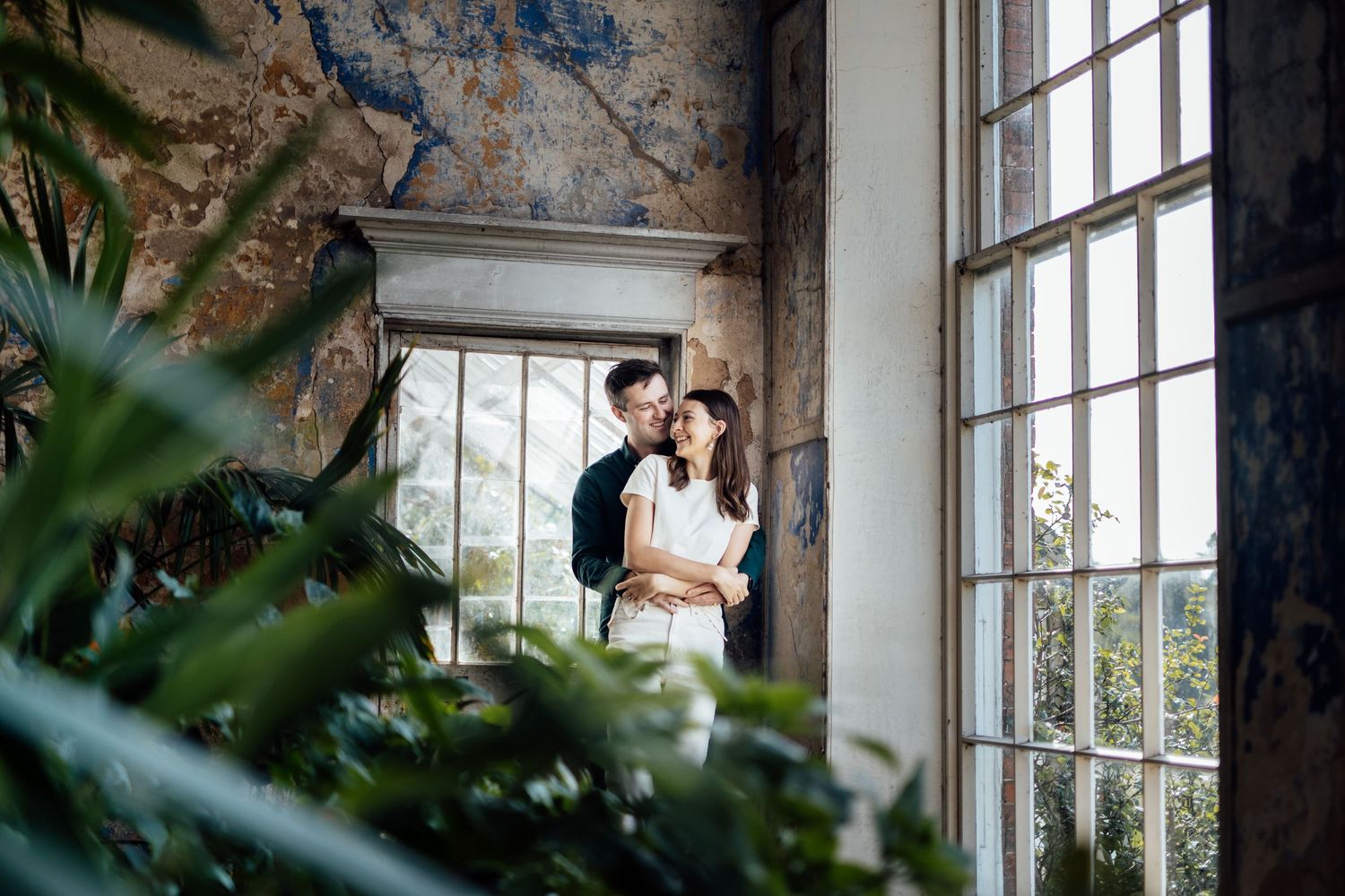 A romantic couple shares an intimate moment by a sunlit window in a rustic building interior.