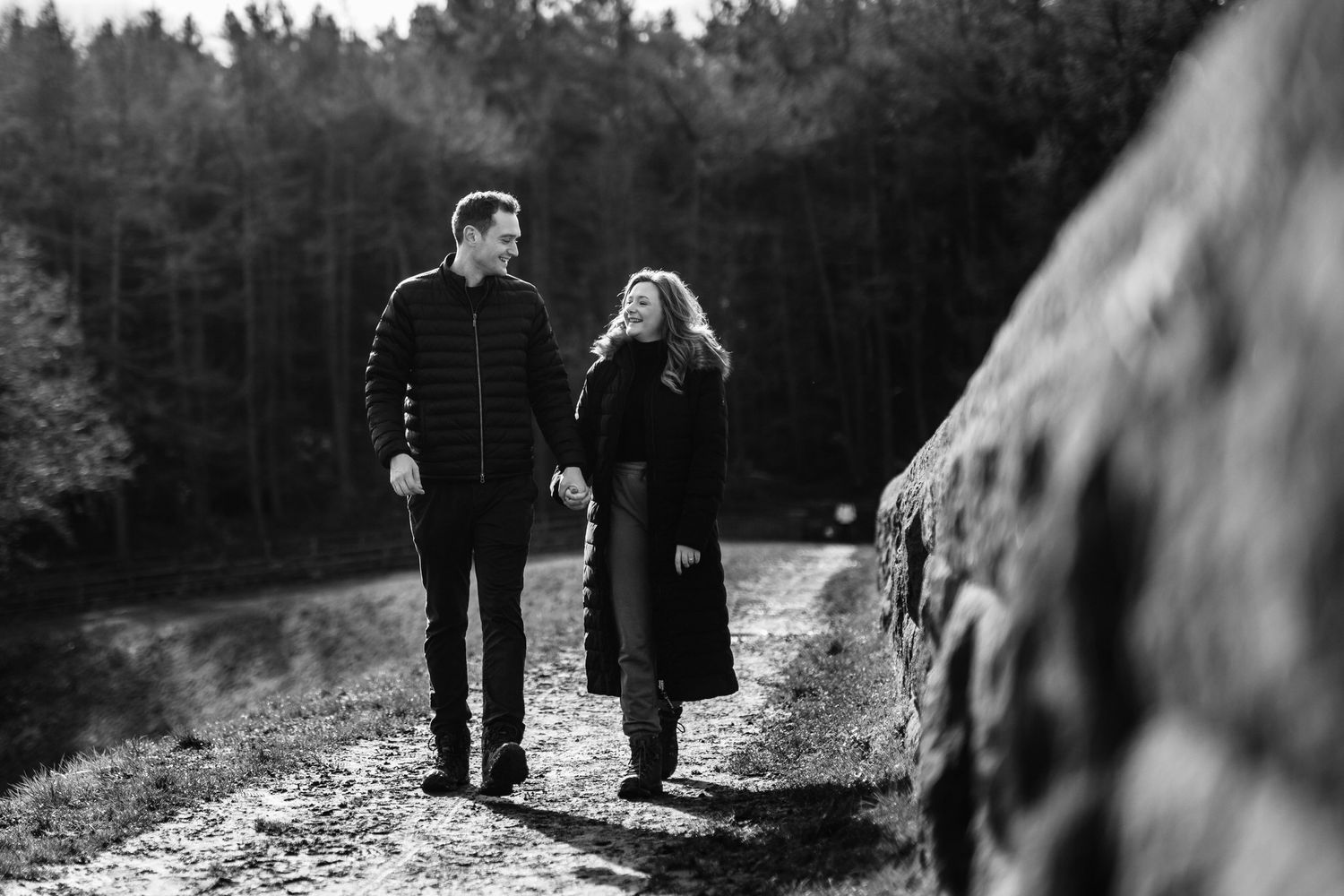 Romantic couple walking through a misty forest path during golden hour.