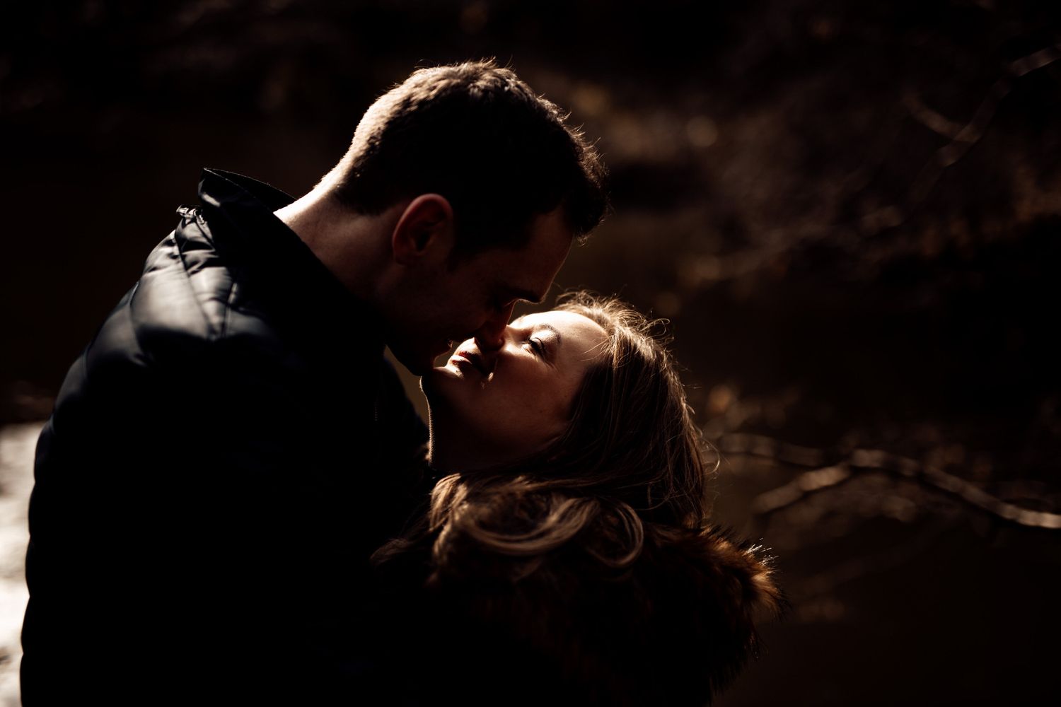 Dramatic silhouette portrait of a couple in an intimate moment against dark shadows.