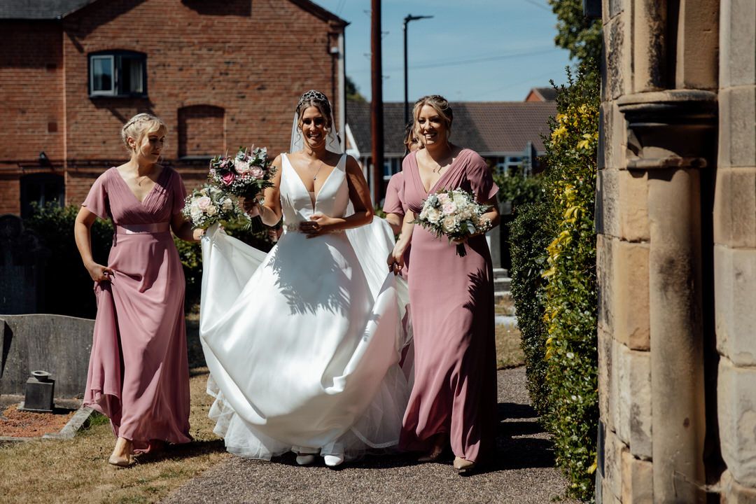 Wedding party poses outside historic brick building with stone columns and archways.