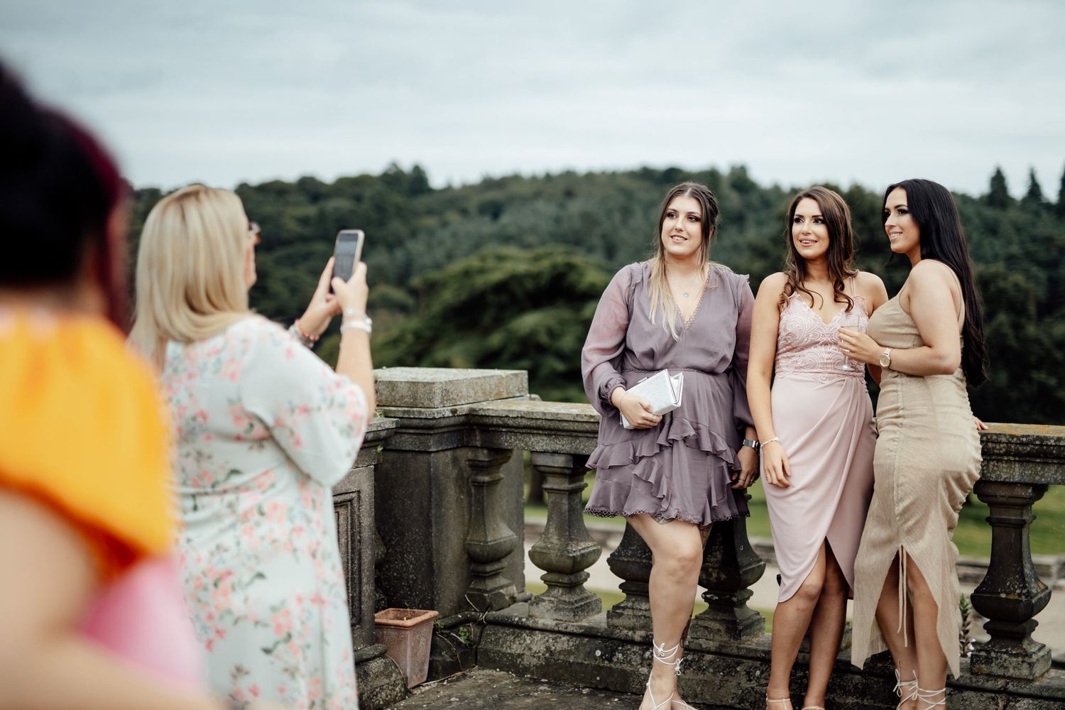 Wedding party in soft pastel dresses gathered outdoors at scenic estate venue.