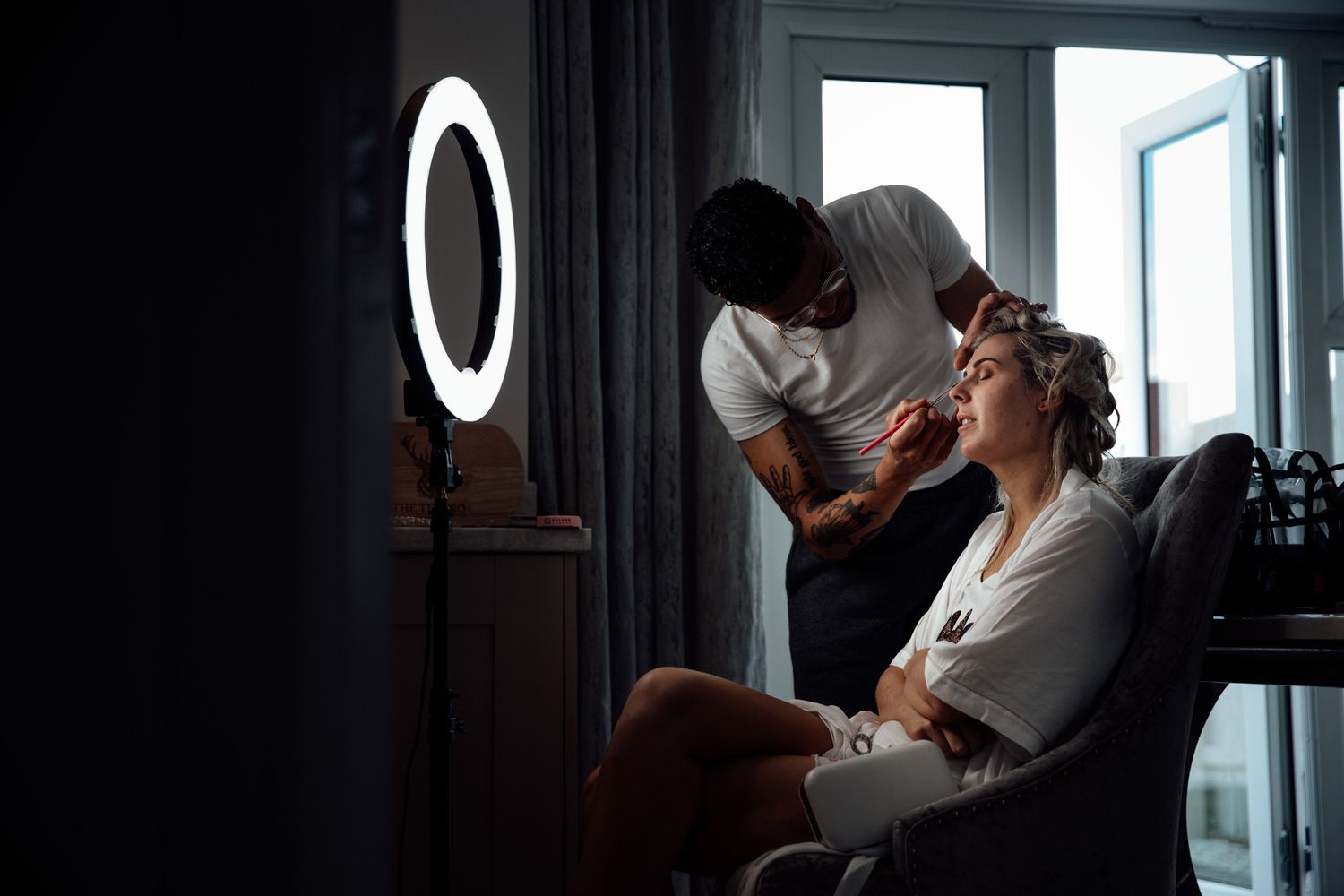 Sunlight streams through window during intimate wedding preparation moment.