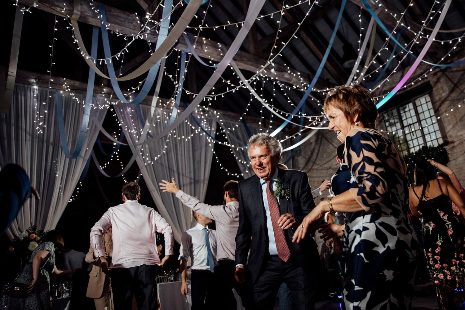 Party guests dance and celebrate under twinkling lights and white fabric draping.