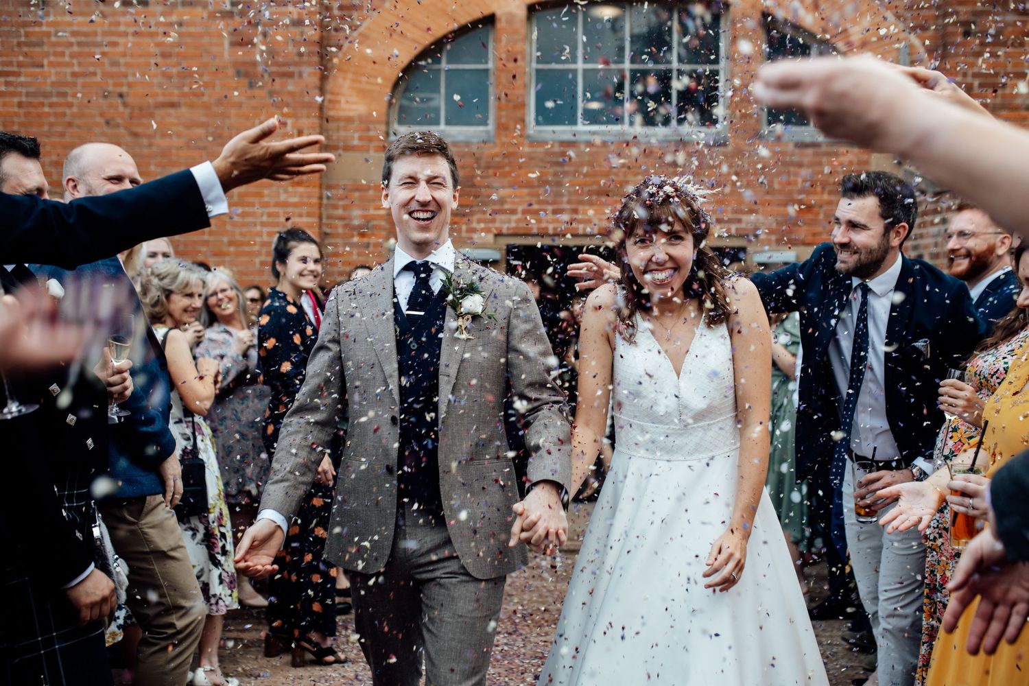 Wedding guests celebrating with confetti outside a rustic brick building.