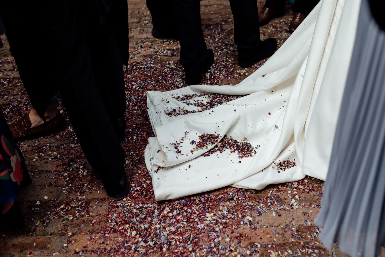 Red confetti scattered on the ground around a white wedding dress train.