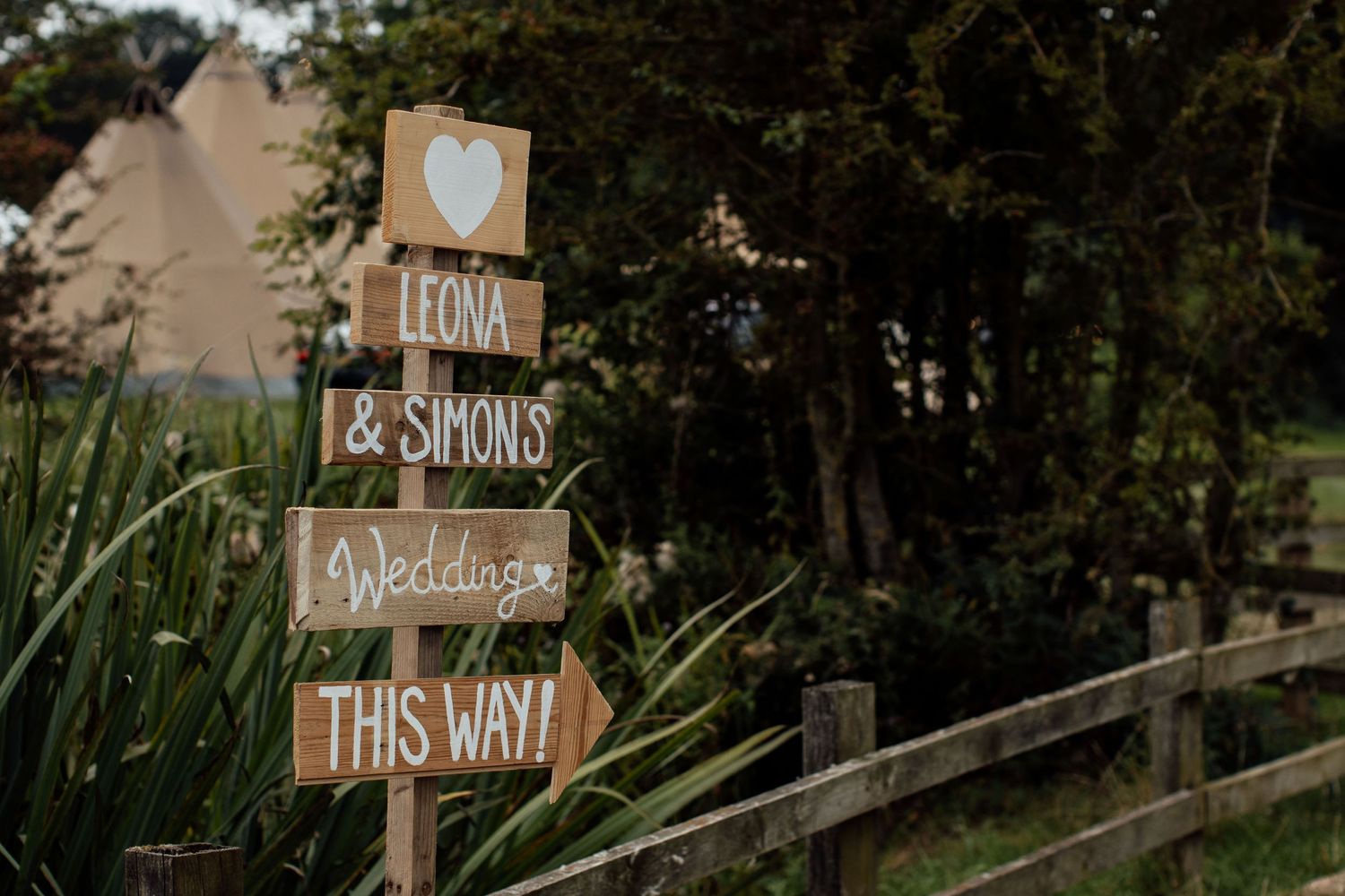Rustic wooden wedding directional signs mounted on posts in a garden setting.