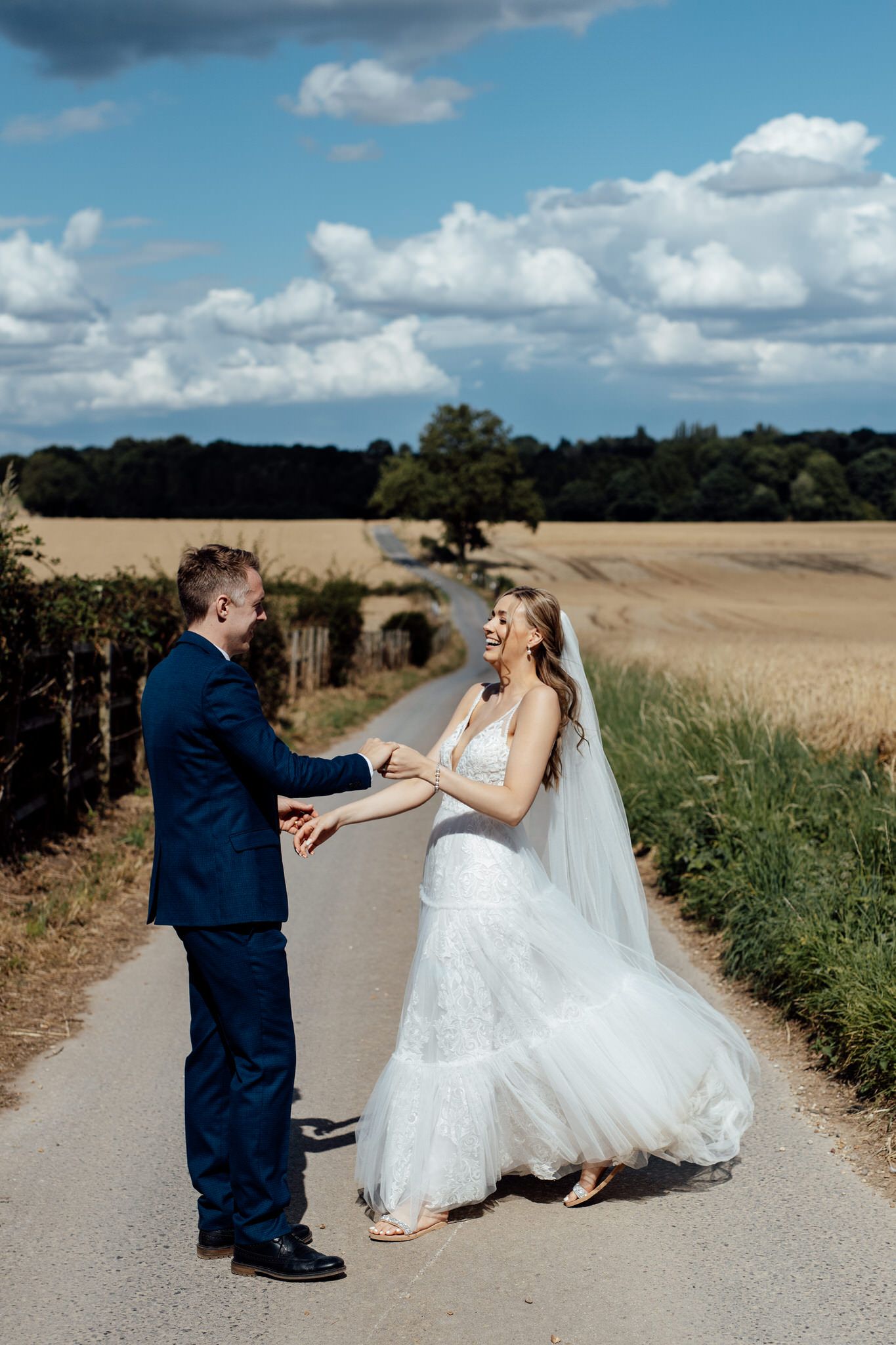 Playful wedding photos taken on a rural path with wheat fields in the background.