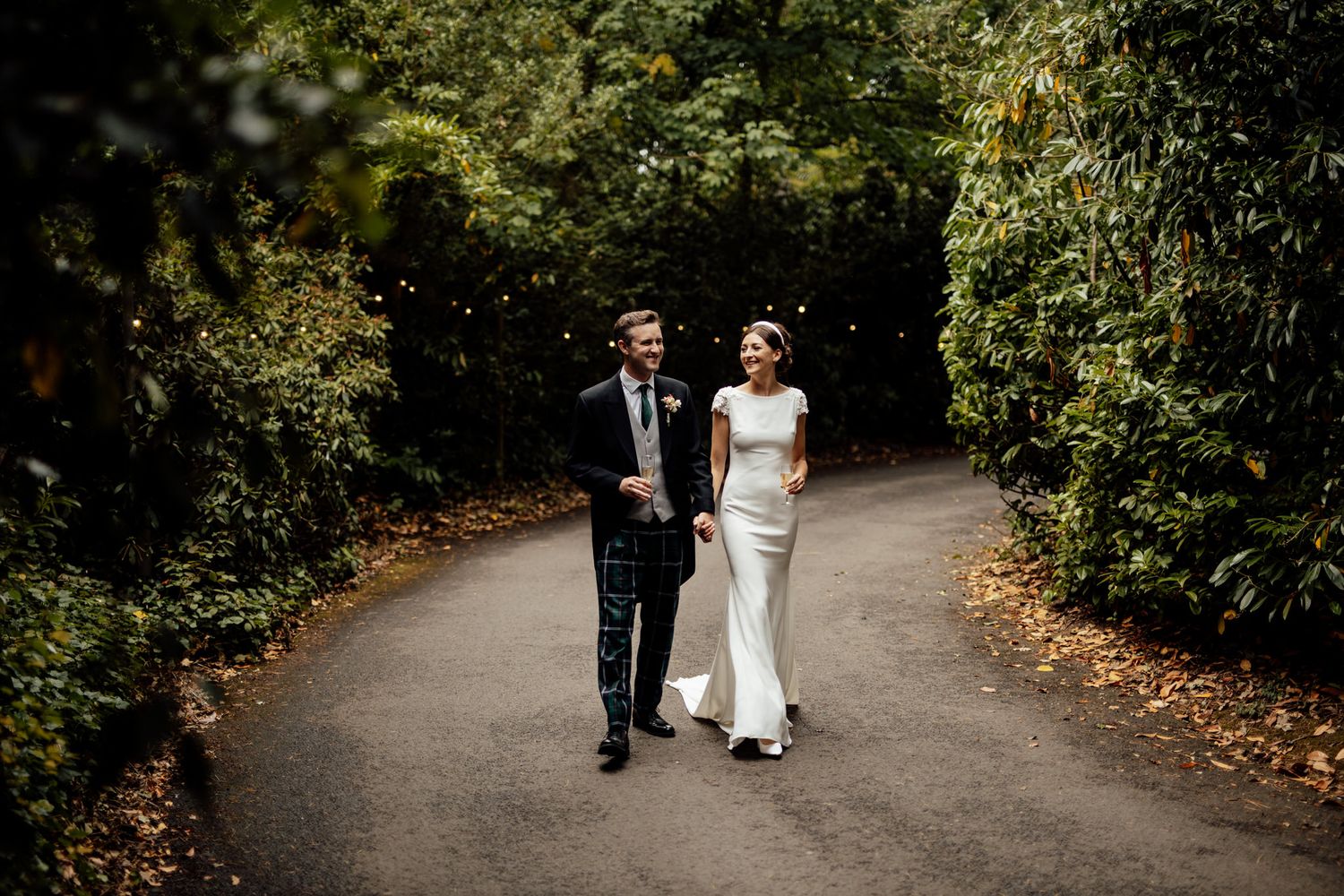 Couple walking along a tree-lined path during an autumn wedding photoshoot.