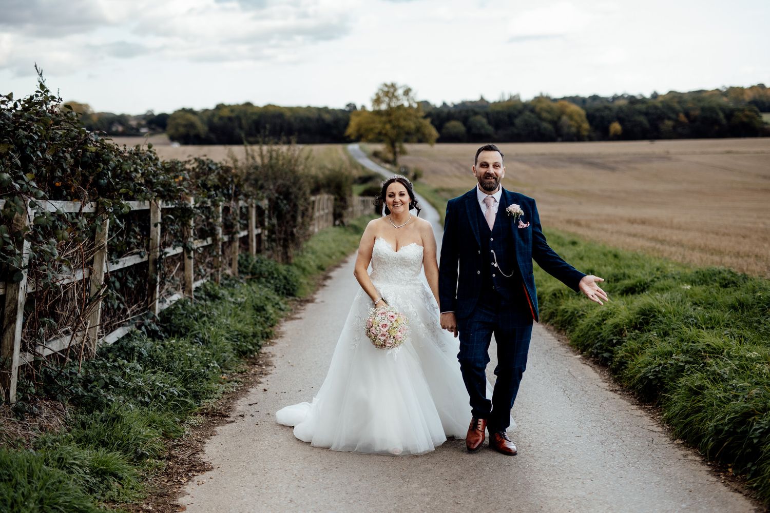 Romantic countryside wedding photos with couple walking along rural path.