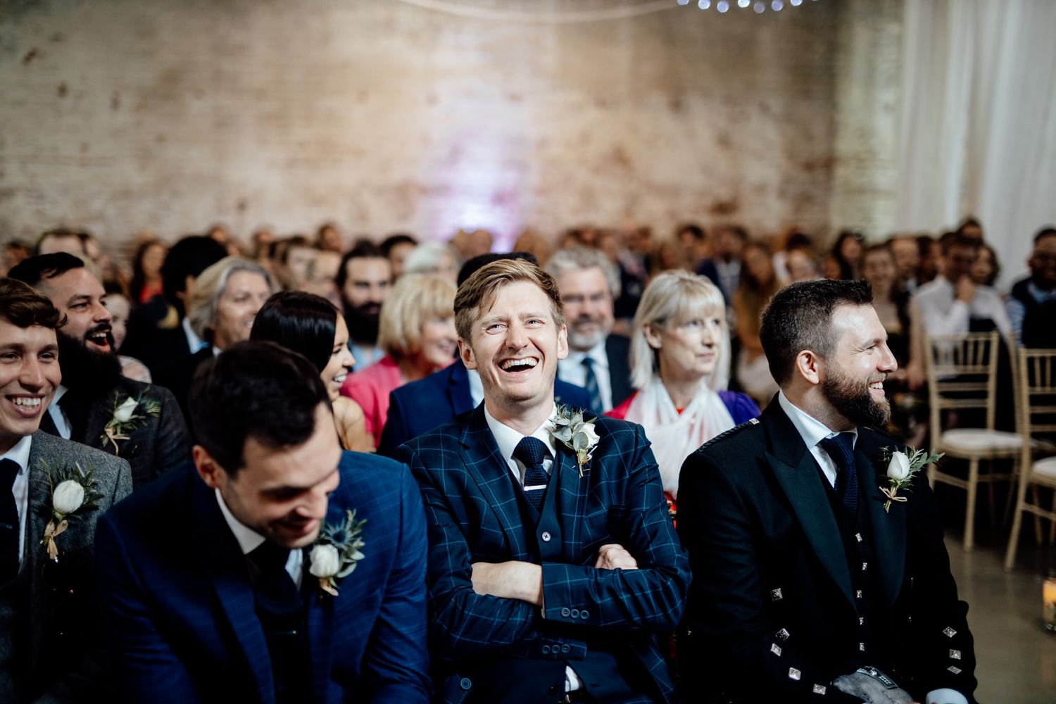 Wedding ceremony audience seated in rows at an indoor venue with brick walls.