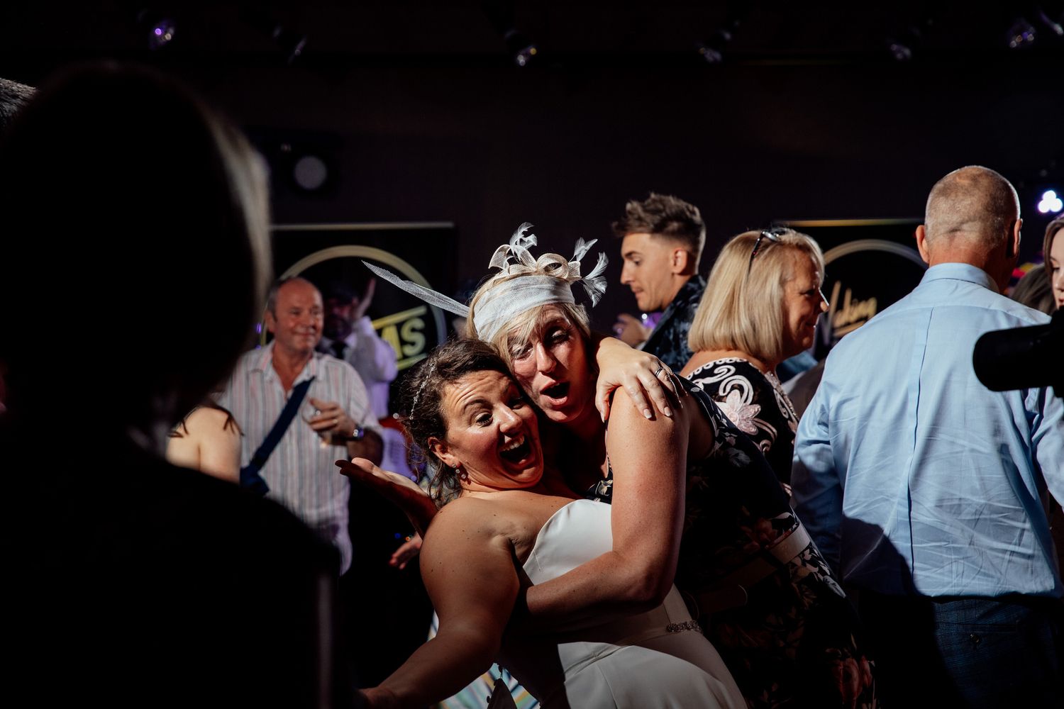 Wedding guests dancing and celebrating on a dimly lit dance floor at a reception.