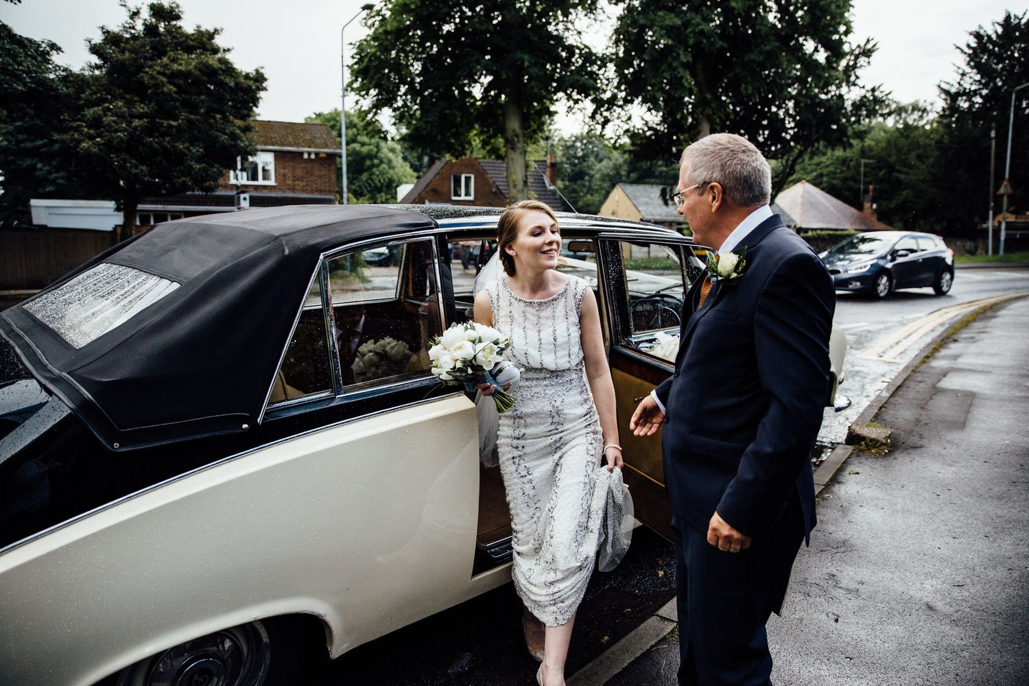 Wedding couple and guests interacting near a vintage car outside.