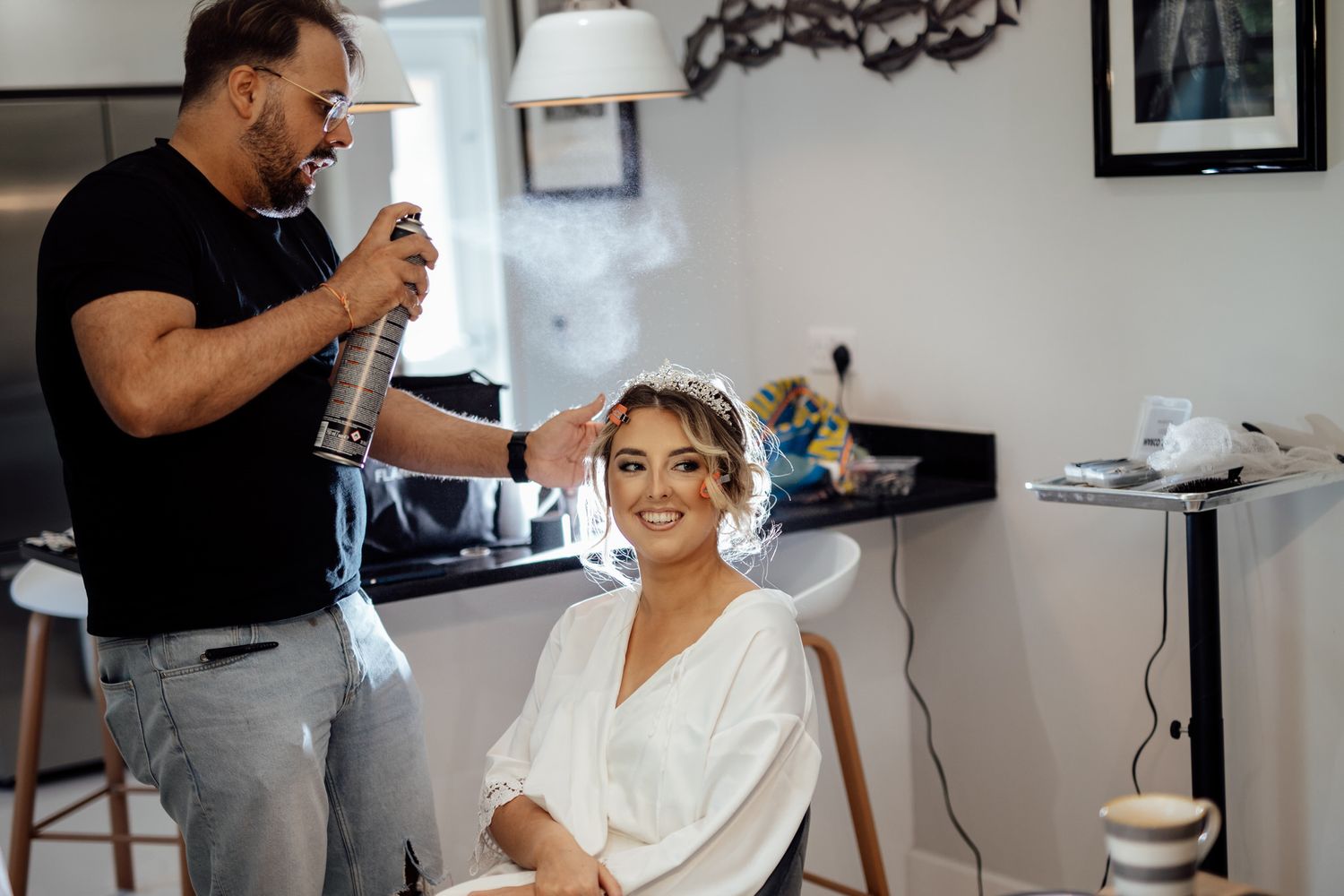 Wedding preparation scene in a bright room with makeup and styling taking place.