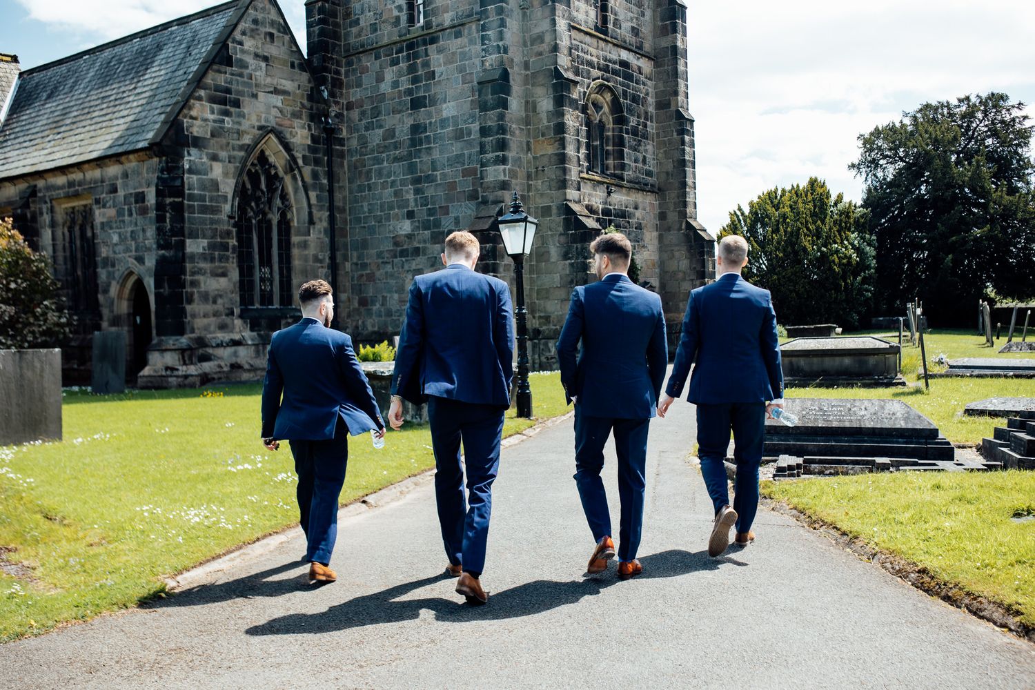 Wedding party walking along stone church pathway in navy suits.