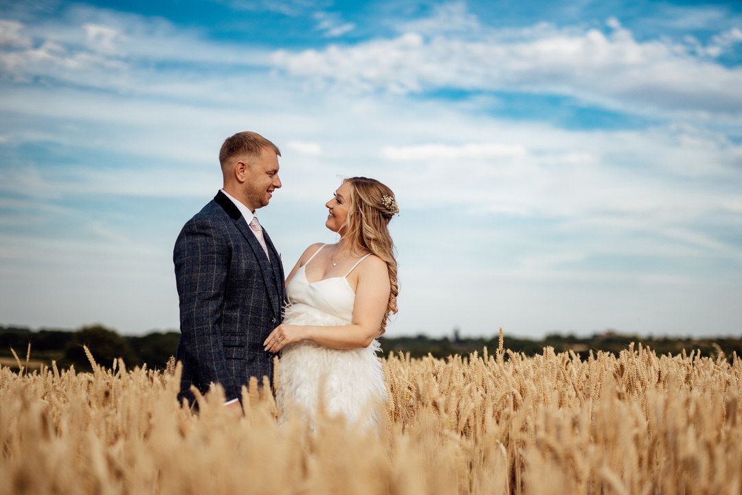 Wedding portraits in golden wheat field with dramatic blue sky backdrop.