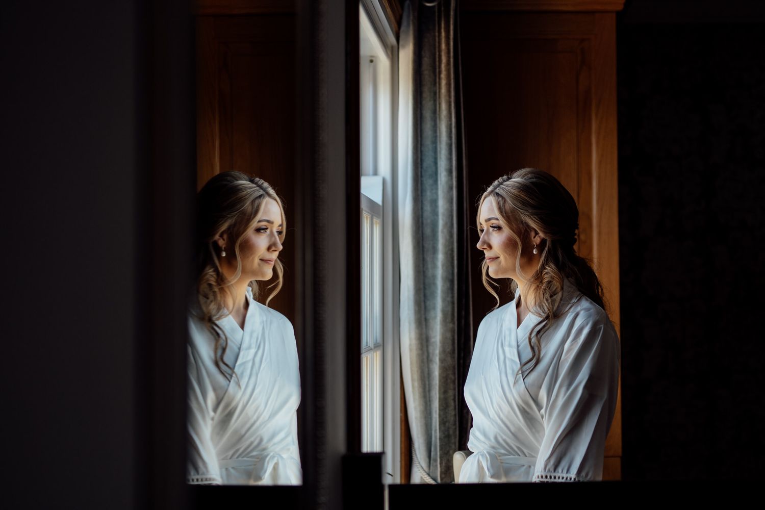 A woman in a white robe stands near a window in moody lighting creating a dramatic silhouette effect.