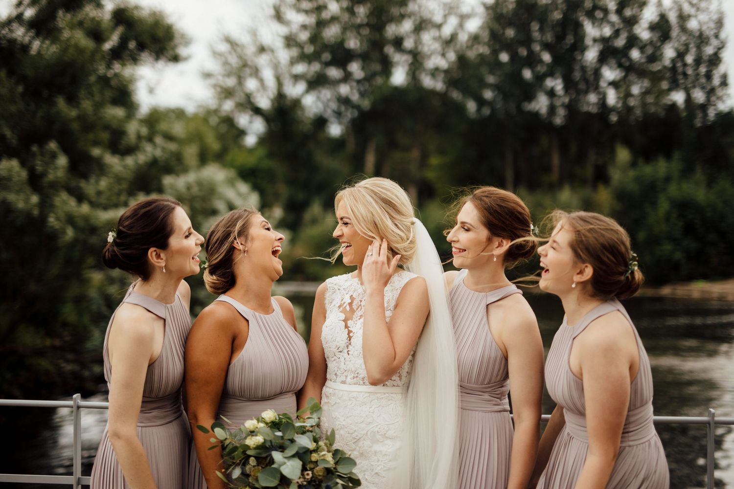 Wedding party standing together outdoors with matching mauve dresses and bouquets.