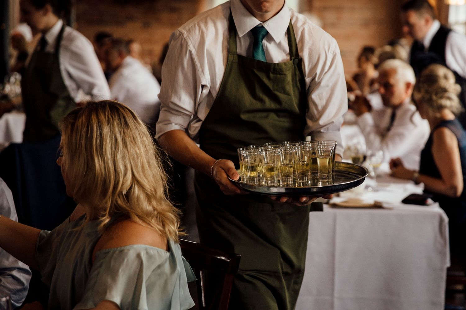 Wedding reception servers carrying trays of drinks through dining room.