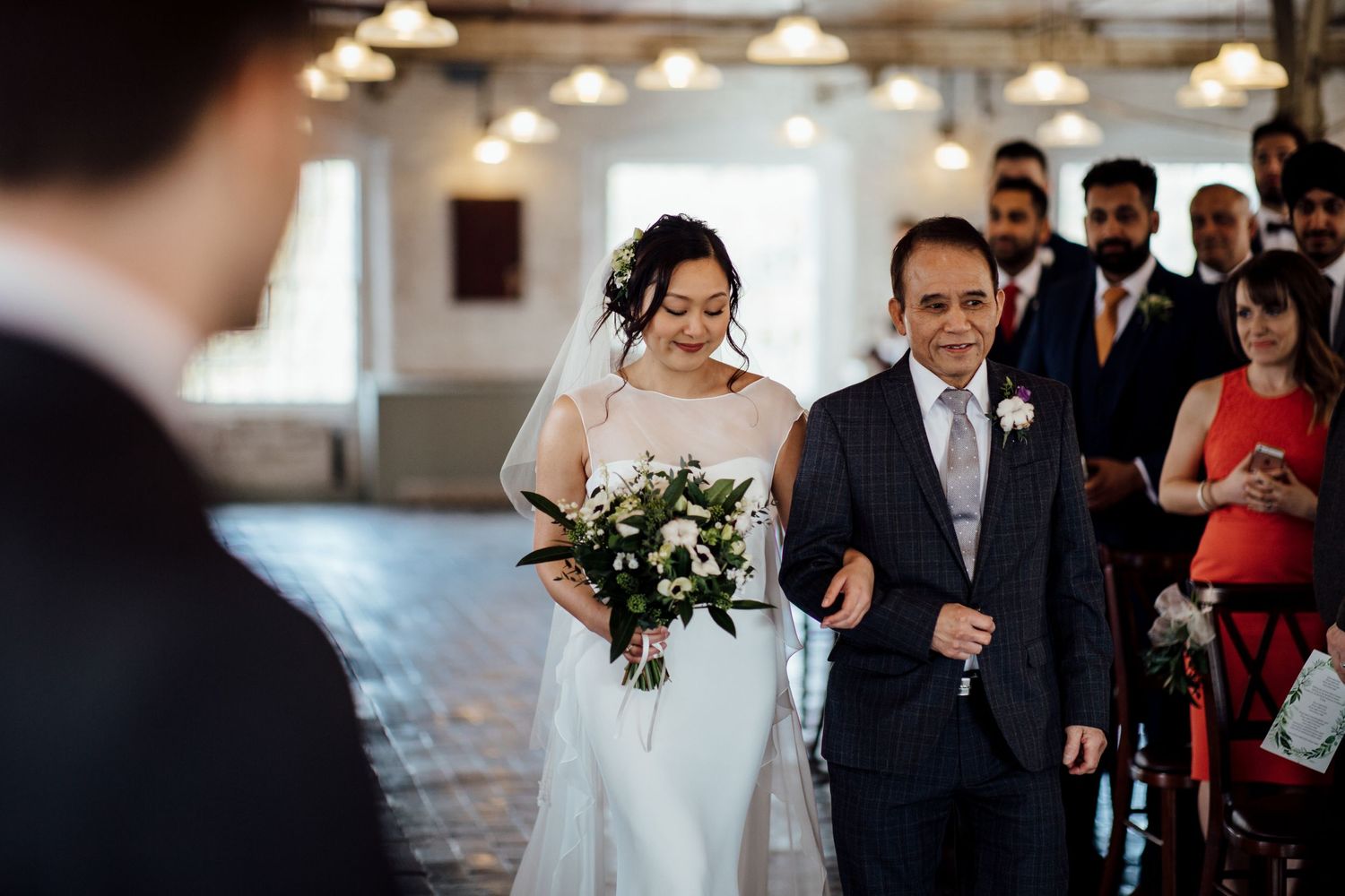Wedding processional in modern venue with industrial lighting fixtures.