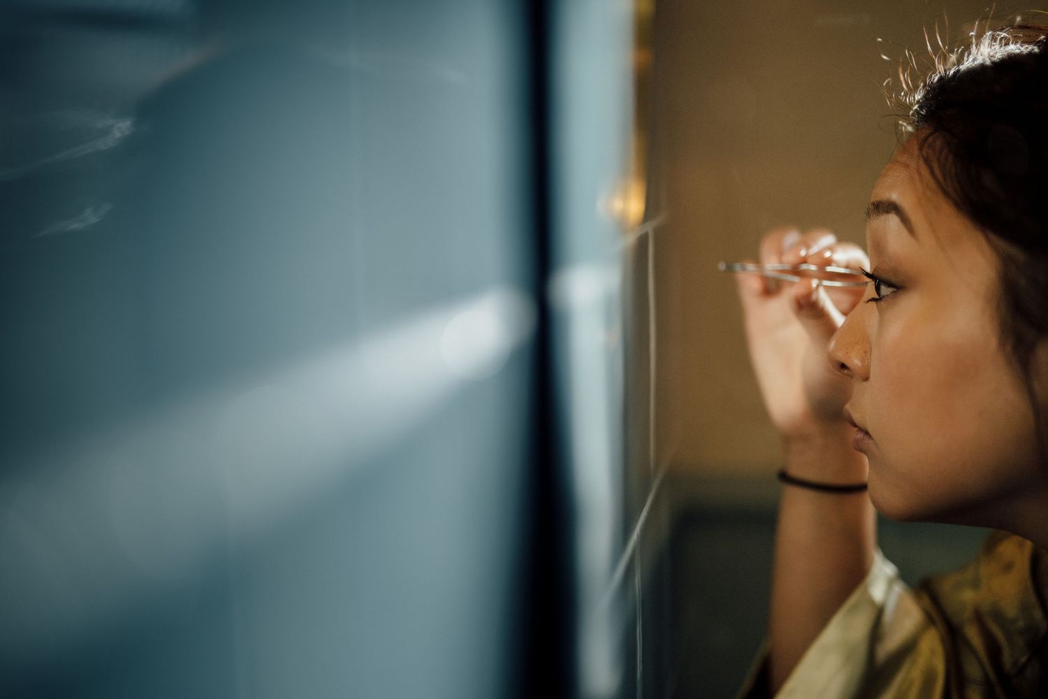 Person applying makeup in soft lighting with blurred background.