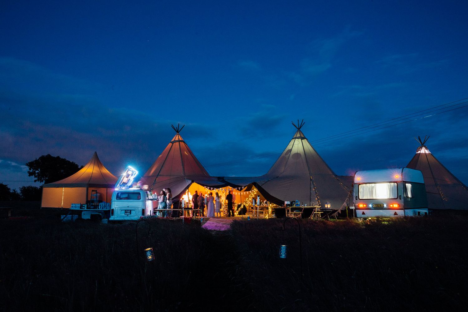 Illuminated glamping tents and structures create a magical nighttime scene against a deep blue sky.
