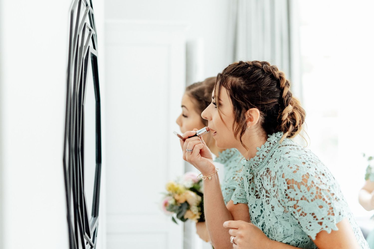 Bridesmaids in matching mint green lace dresses getting ready in a bright white room.