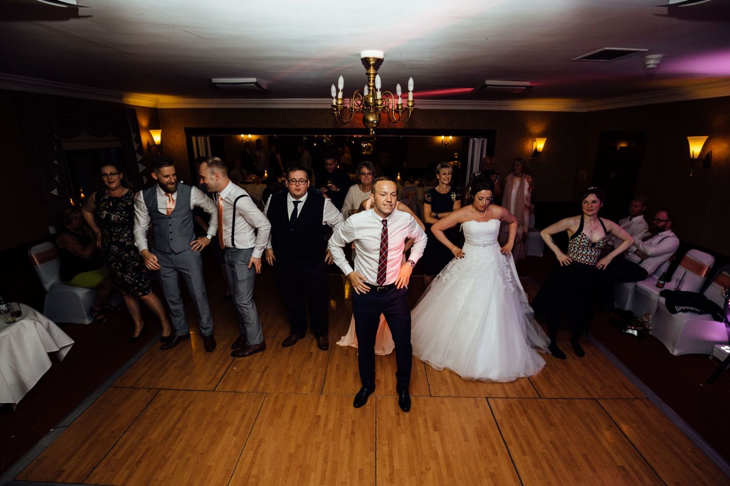 Wedding reception dance floor with warm lighting and guests celebrating in formal attire.