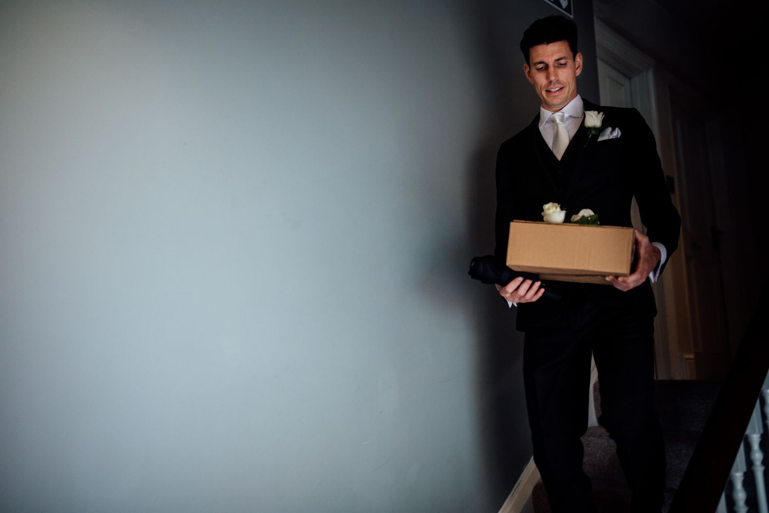 Person in formal attire holding box in dimly lit hallway.