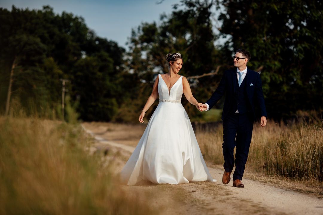 Newlyweds walk together along rustic outdoor trail during summer photoshoot.