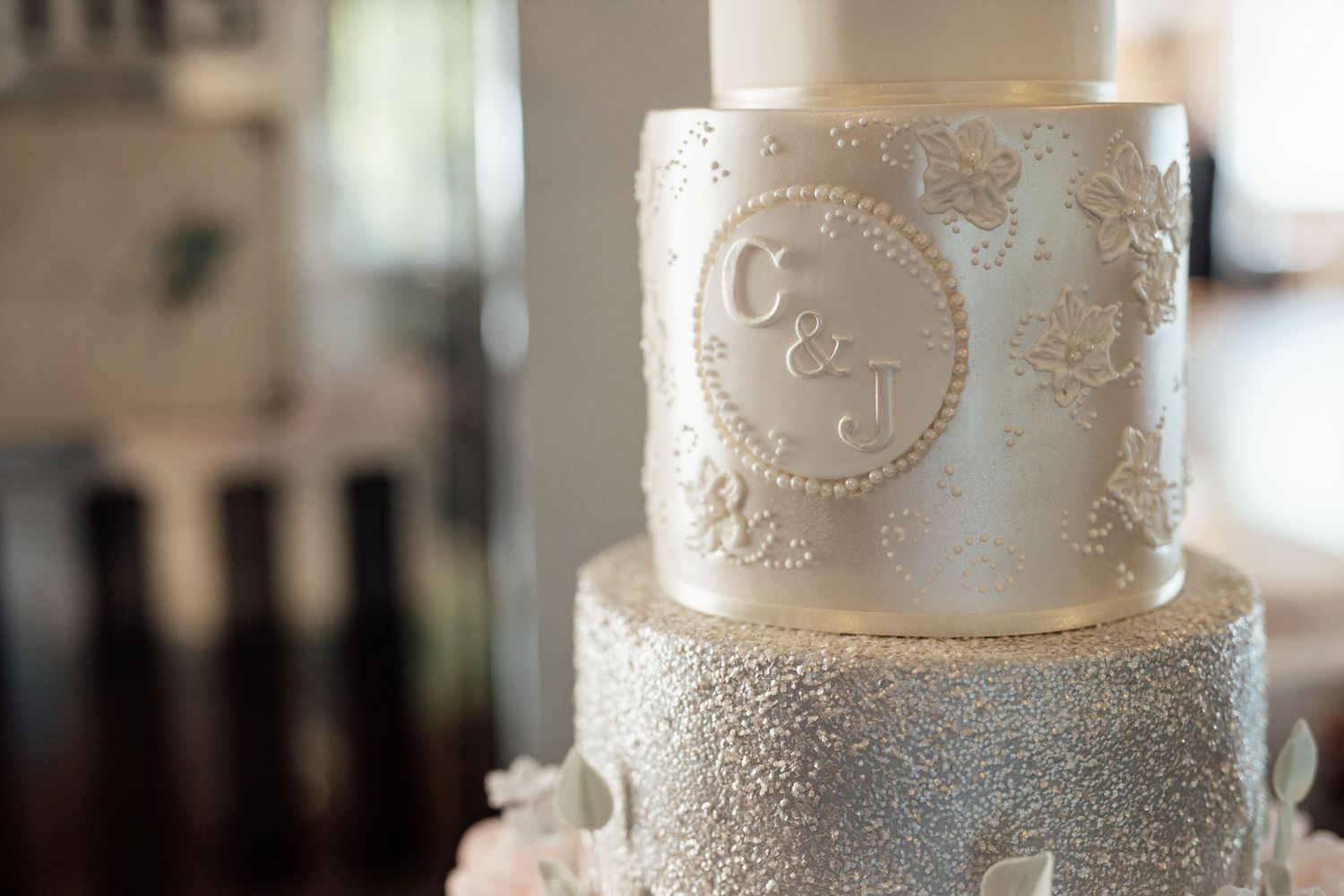 Elegant white wedding cake decorated with silver sparkles and intricate lace patterns.