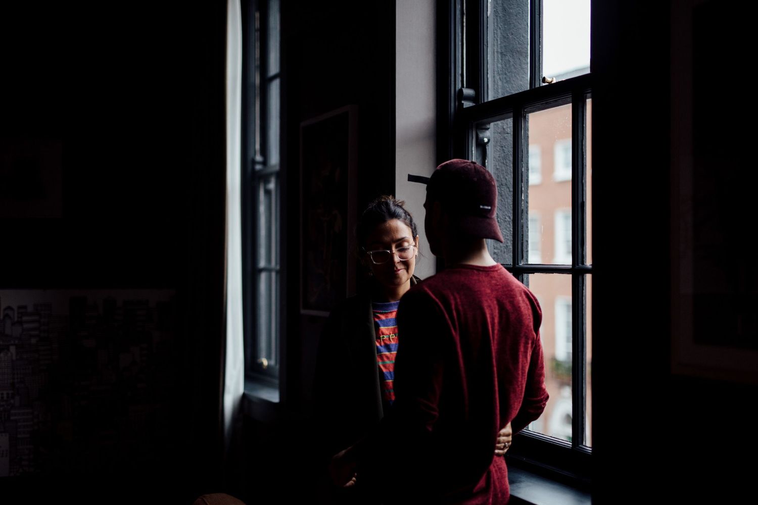 Silhouetted figures near windows in a dark interior space.