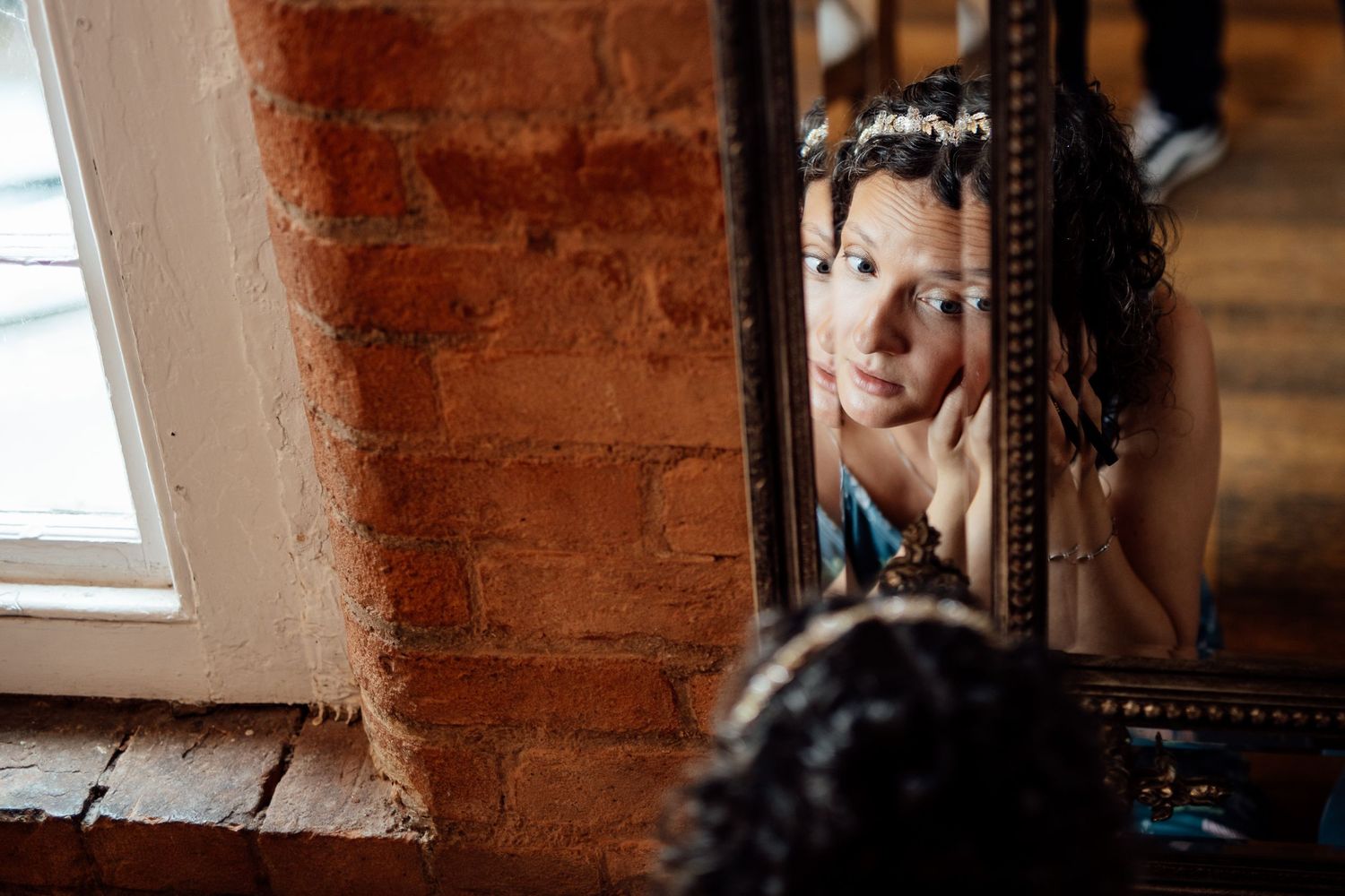 Reflection in an antique mirror against exposed brick wall with natural window light.