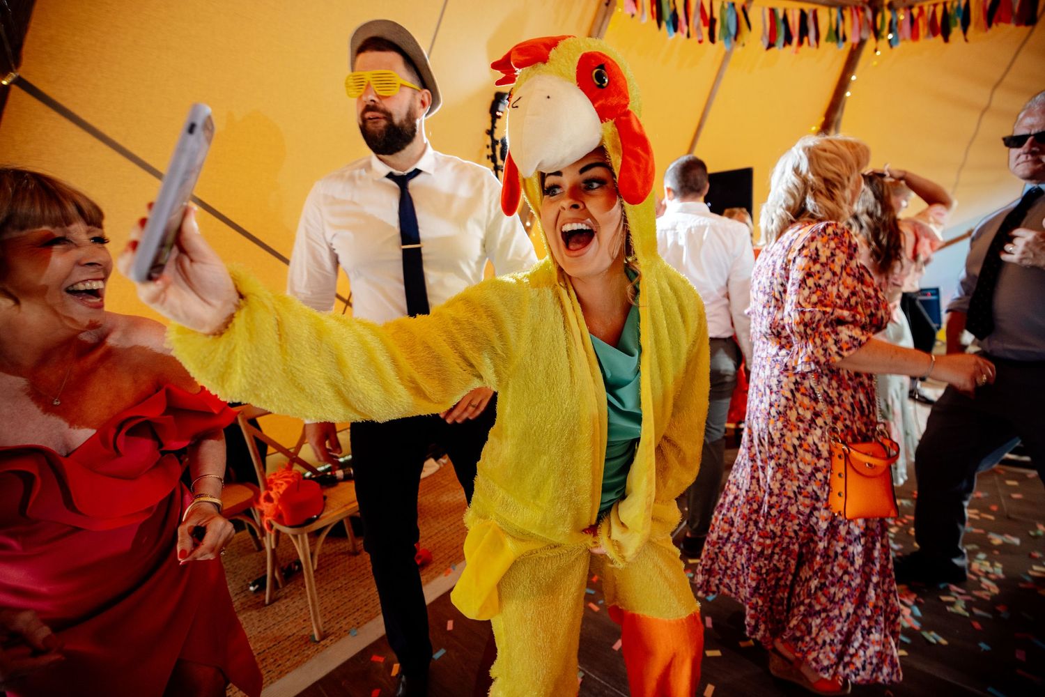 Energetic dance party under orange tent with festive decorations and colorful lighting.