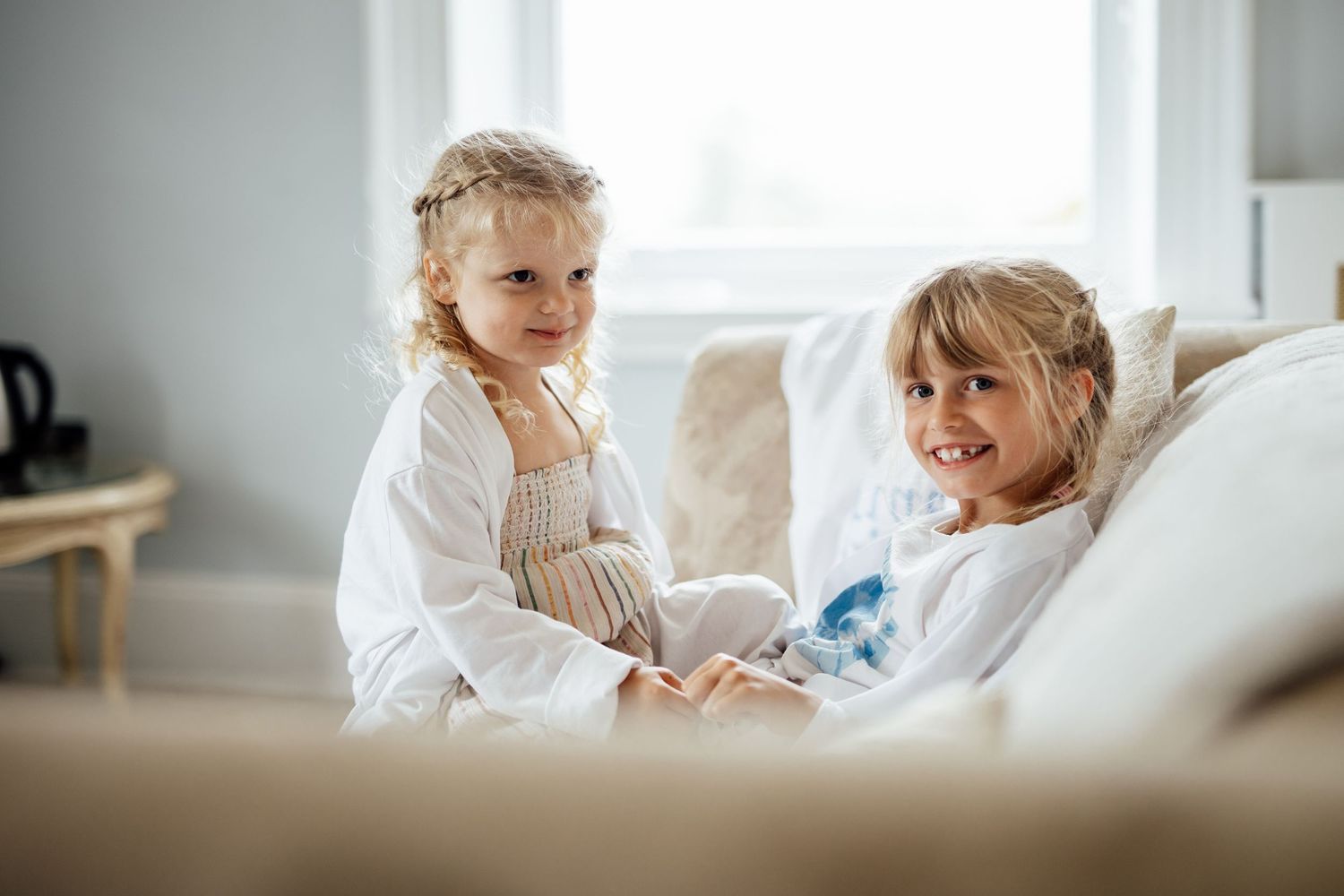 Young children playing together on white bedding in a bright room.
