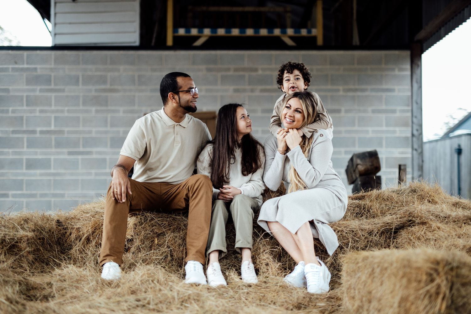 Casual family portrait session on hay bales against rustic barn backdrop.
