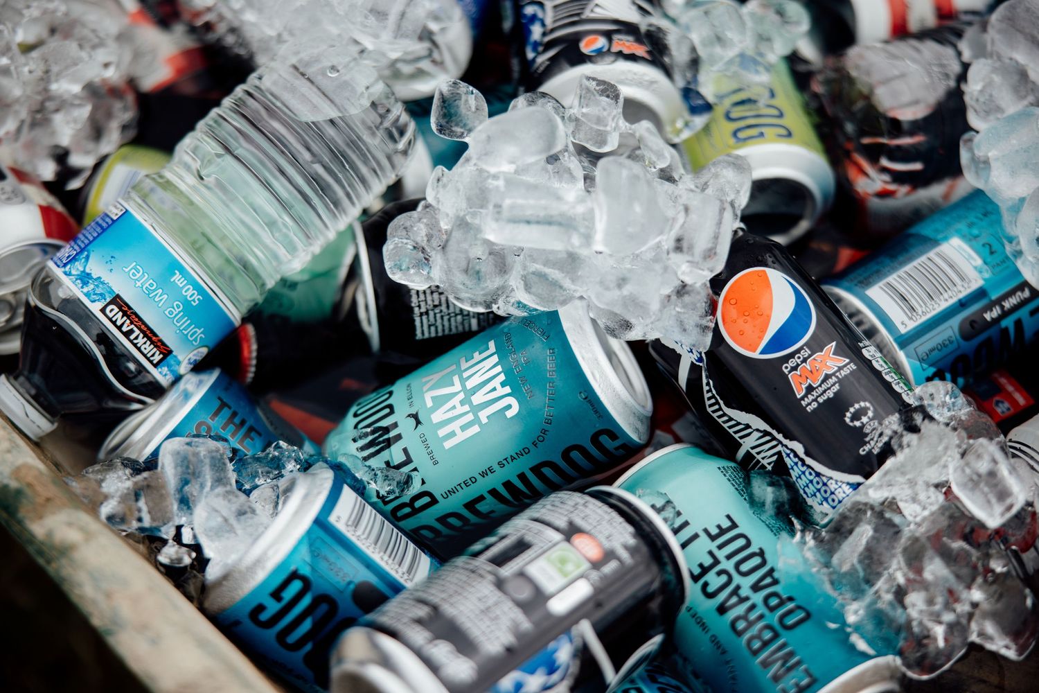 Ice-filled cooler with assorted beer cans and bottles at outdoor event.
