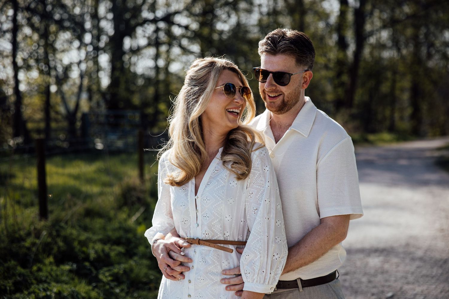 Couple walking together on tree-lined path in matching white outfits.