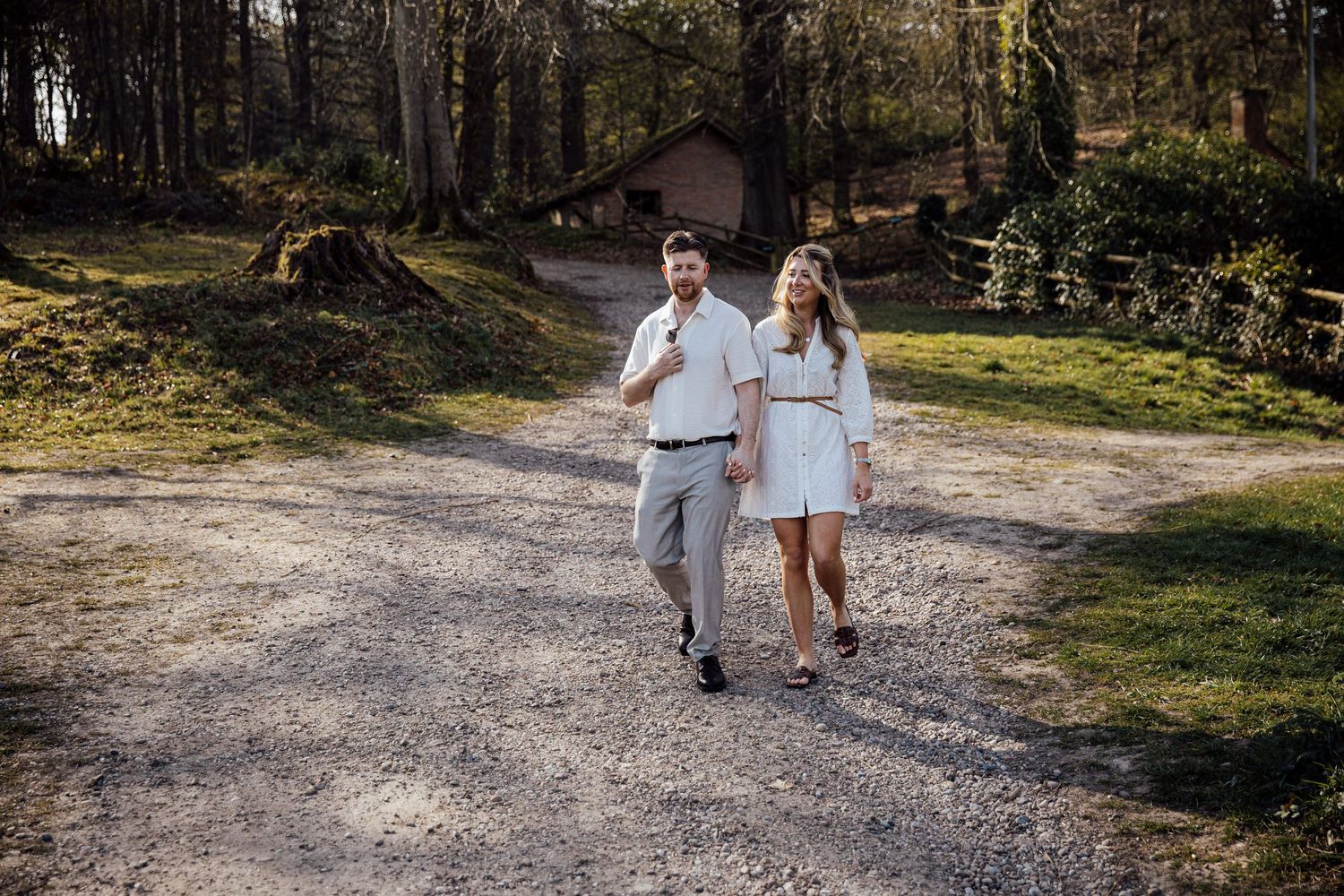 A couple strolling down a gravel path surrounded by lush greenery and trees.