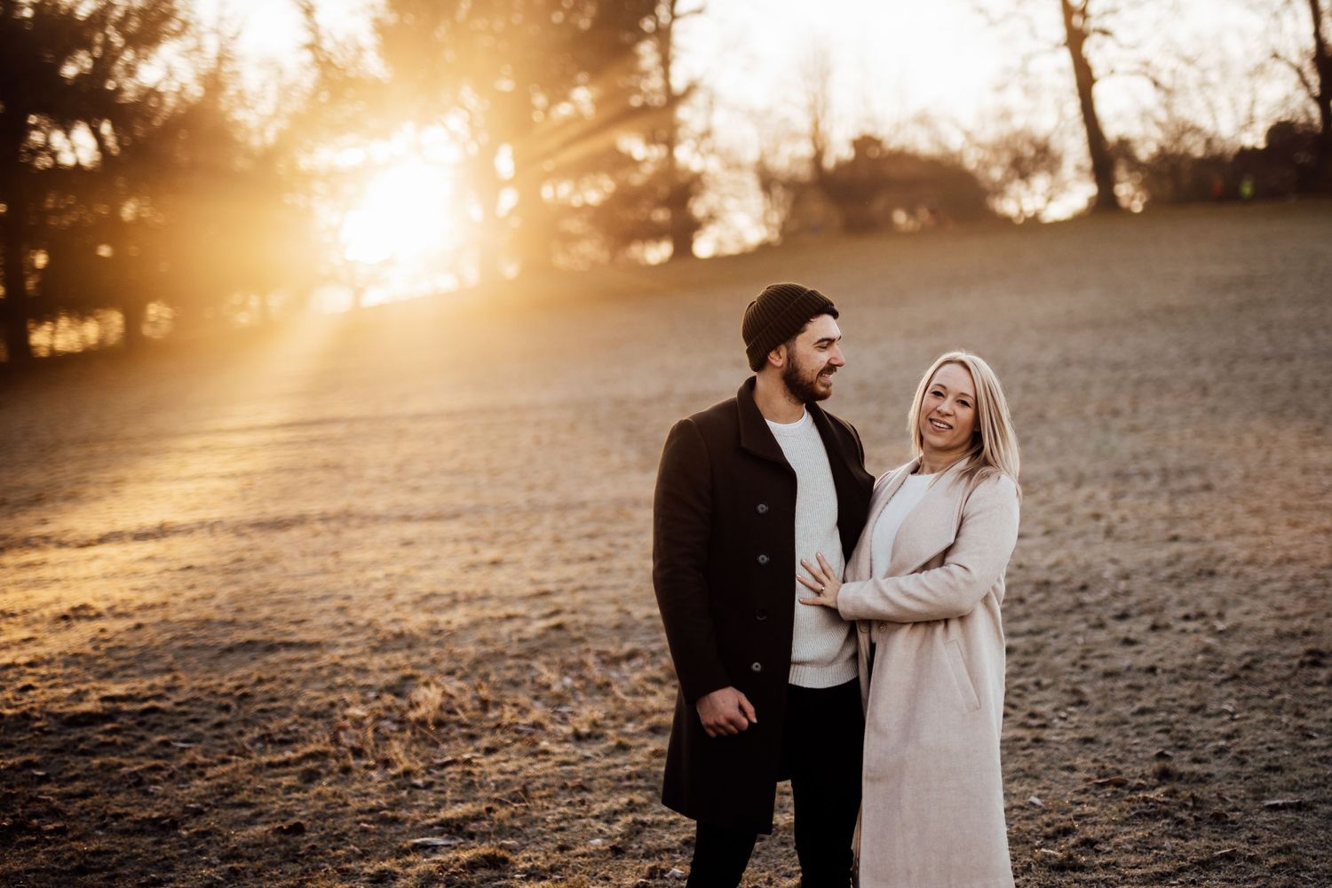 Romantic couple embracing in a golden sunset with trees silhouetted in the background.