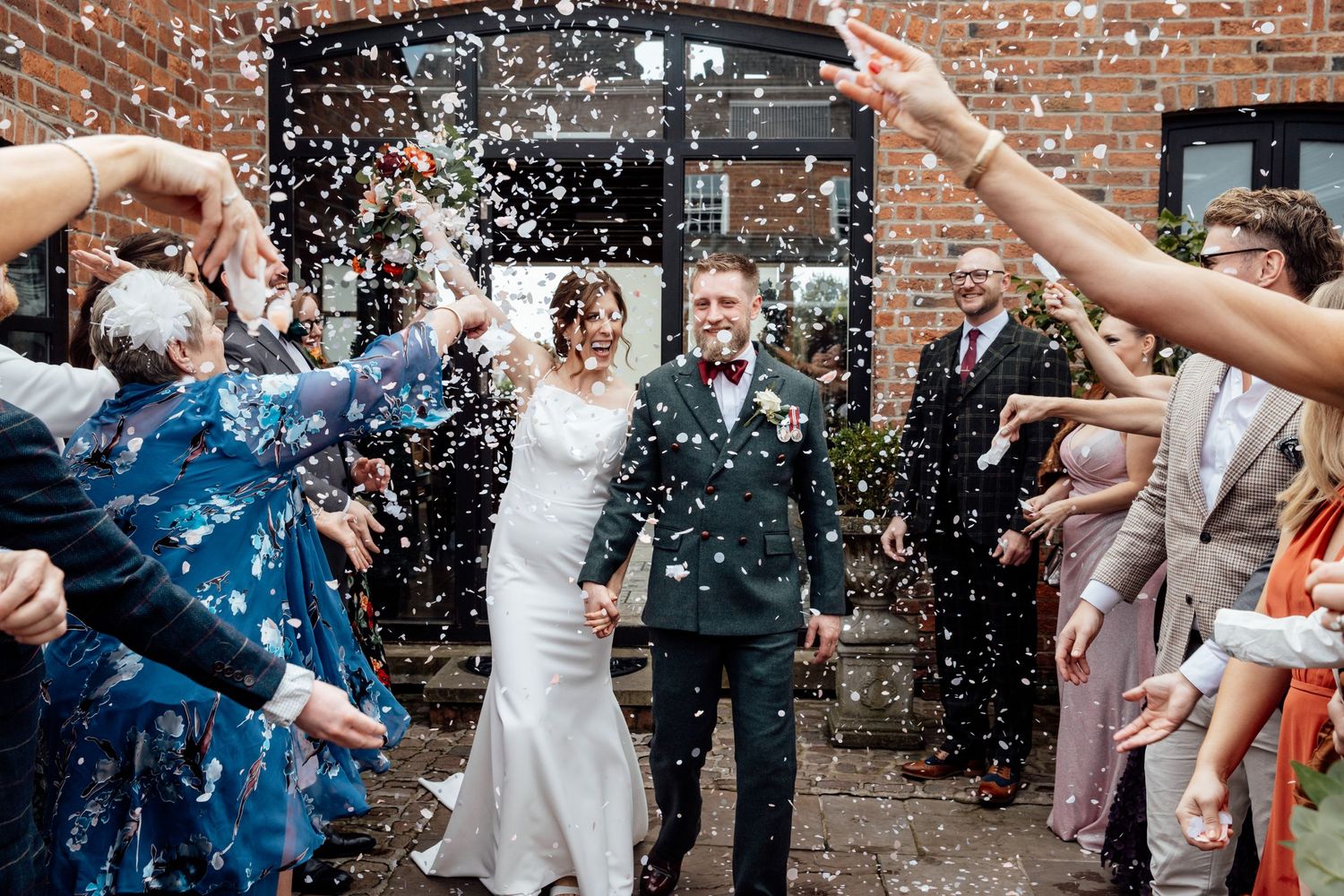 Wedding guests throw confetti at celebration outside brick building.