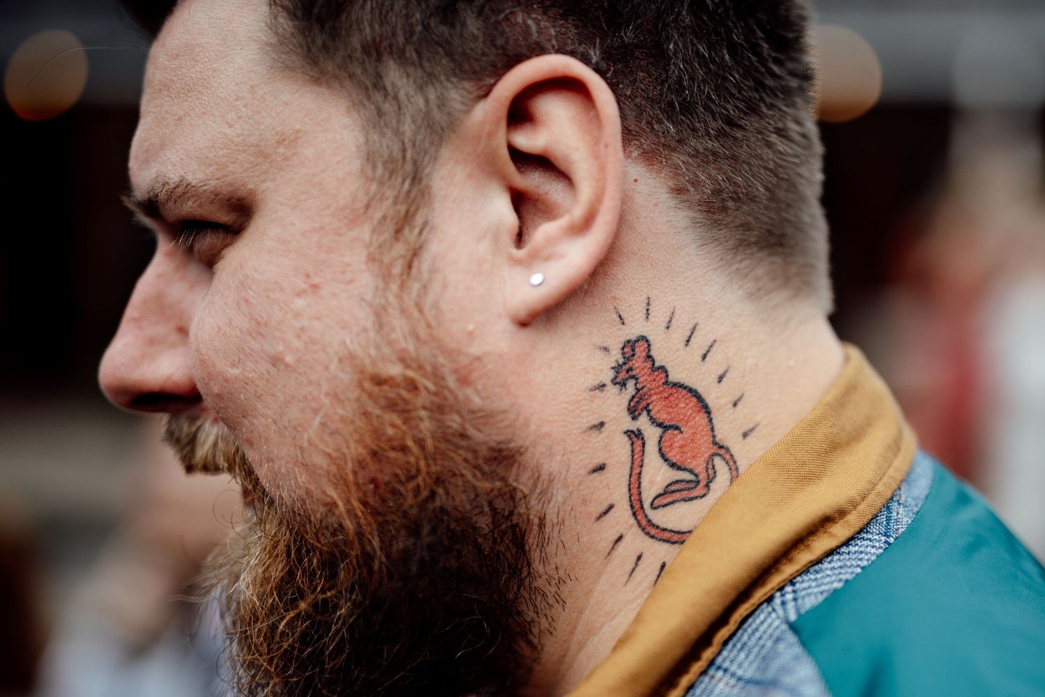 Close-up profile view of a bearded man with a colorful kangaroo neck tattoo.