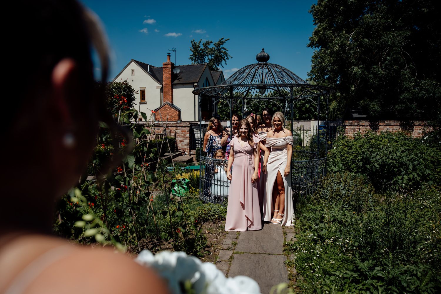 Garden wedding ceremony setup with gazebo and guests in summer attire.