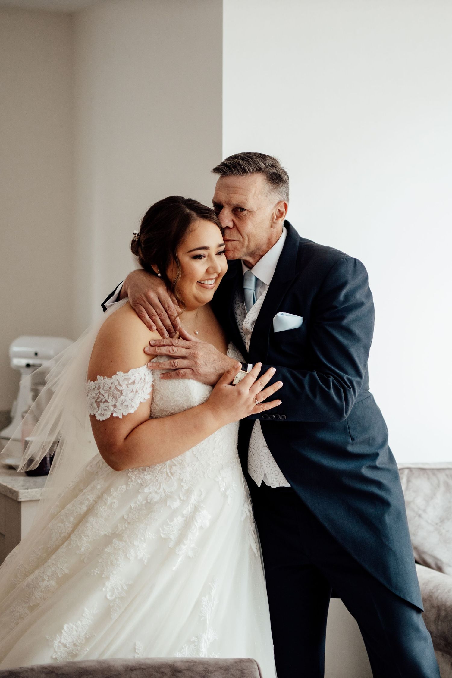 Intimate wedding couple moment captured in bright white room.