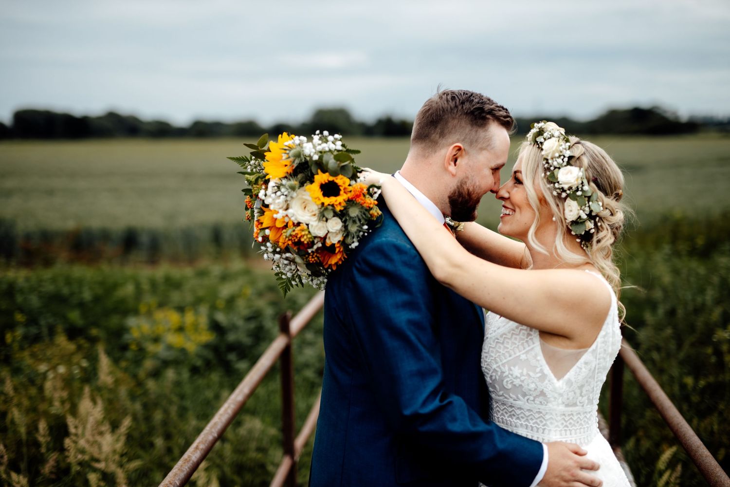 A romantic wedding portrait with sunflowers and floral crown in a countryside setting.