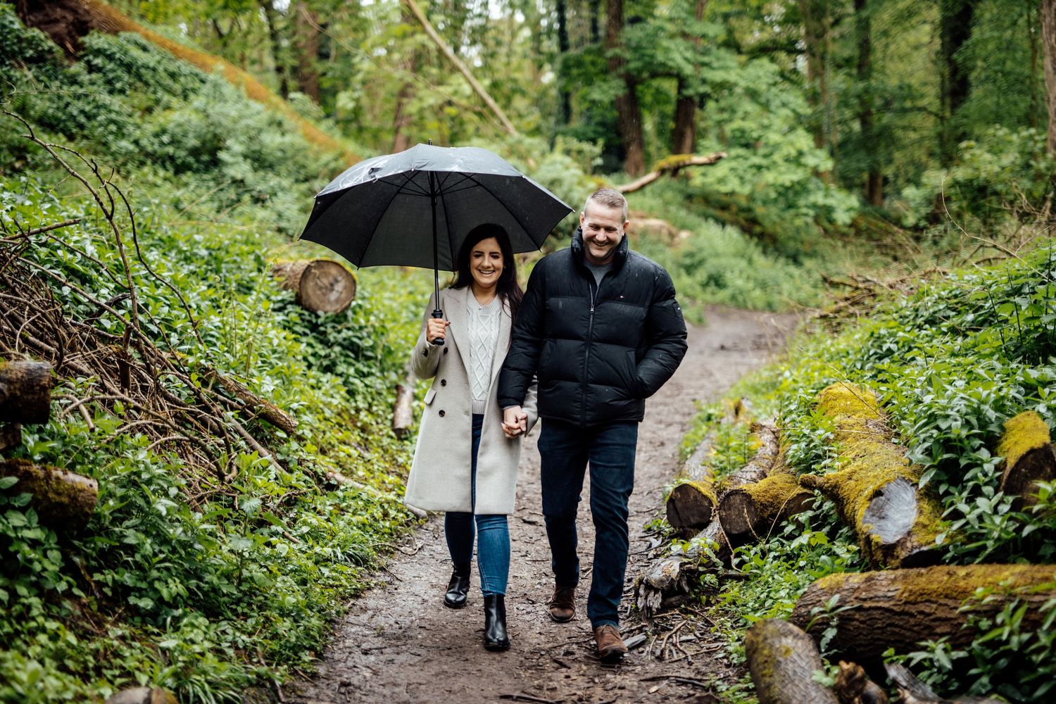 People walking together on a lush green forest trail with umbrellas on a rainy day.