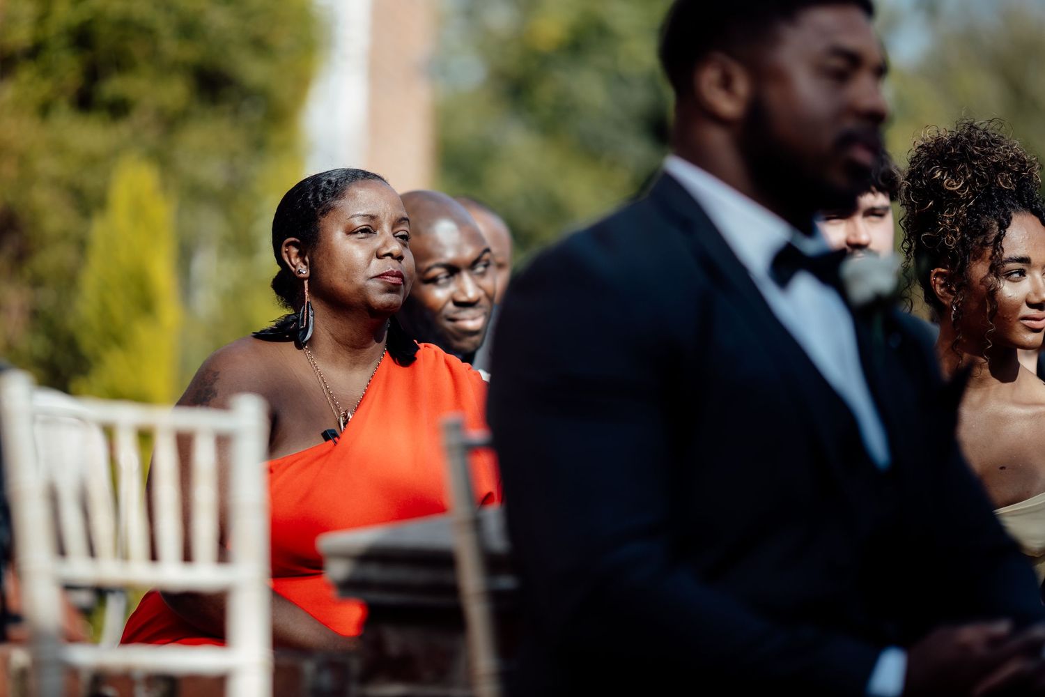 Wedding guests in formal attire seated at an outdoor ceremony.