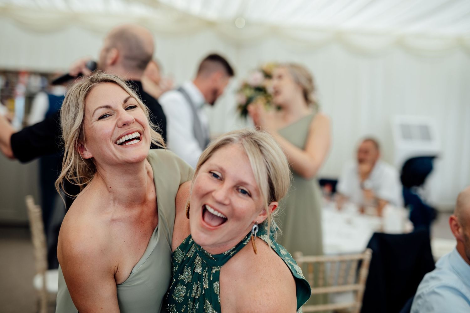 Wedding guests dancing and celebrating under a white tent at an evening reception.