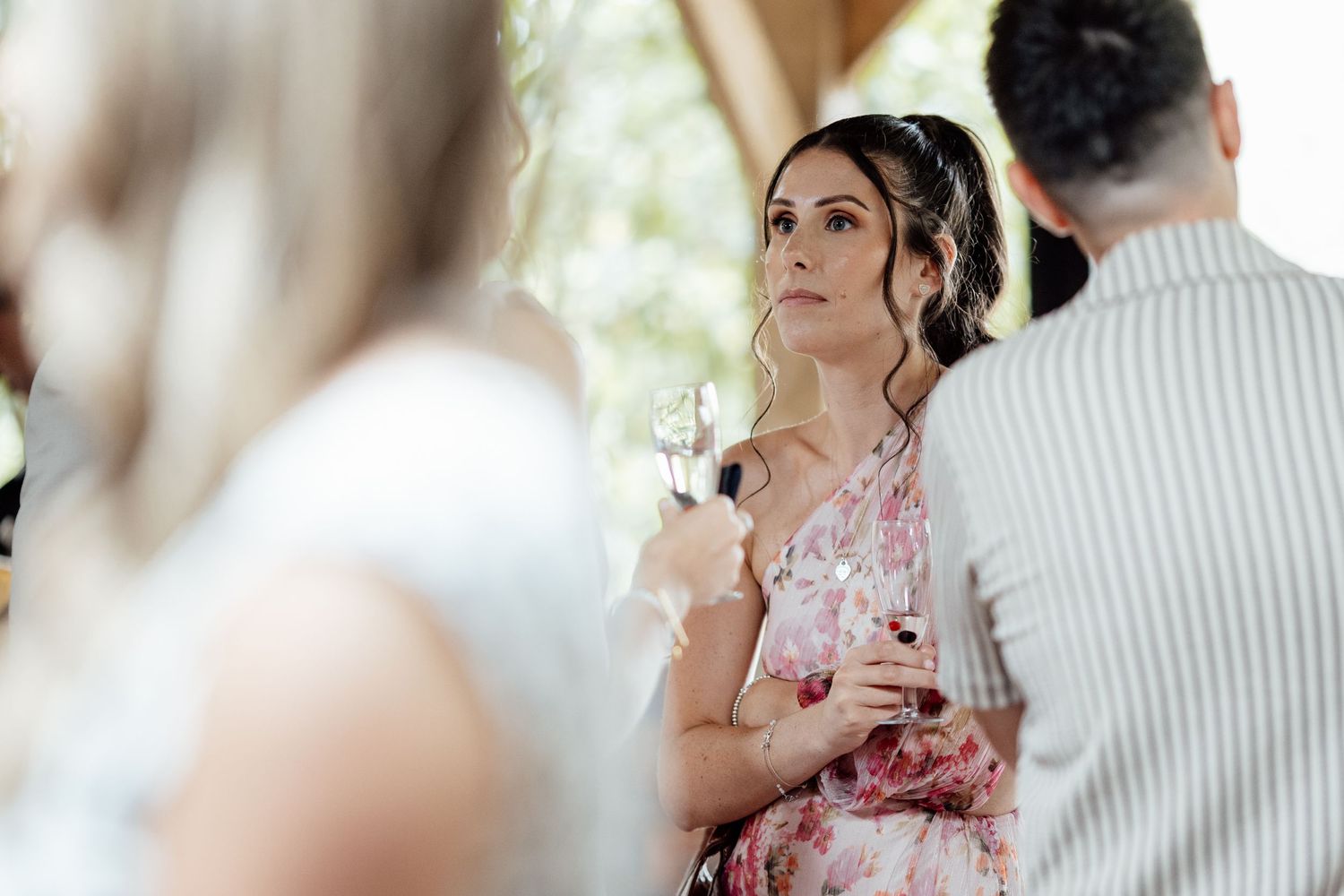 Elegant wedding guest in floral dress holding champagne glass at outdoor garden wedding reception.