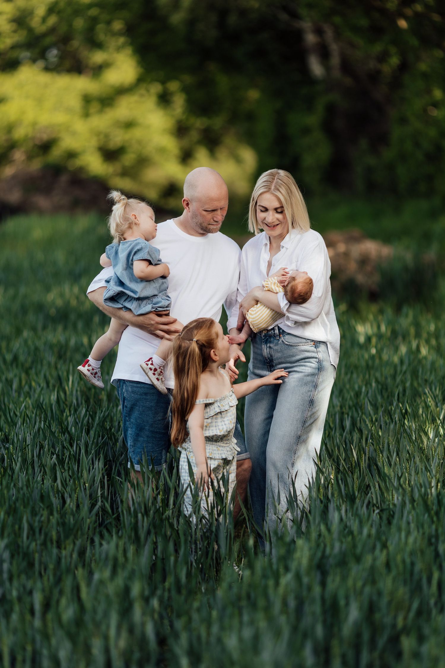 Happy family with three children standing in a lush green field, parents holding babies outdoors.